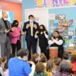 City education leaders do hand movements along with preschoolers while teachers play instruments and lead a song in Spanish
