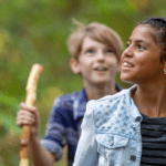 A school-aged youth of color hikes in the forest with peers.