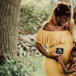 Pregnant Black parent holds ultrasound photo with partner and preschool aged child.