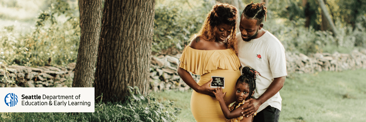 Pregnant Black parent holds ultrasound photo with partner and preschool aged child.