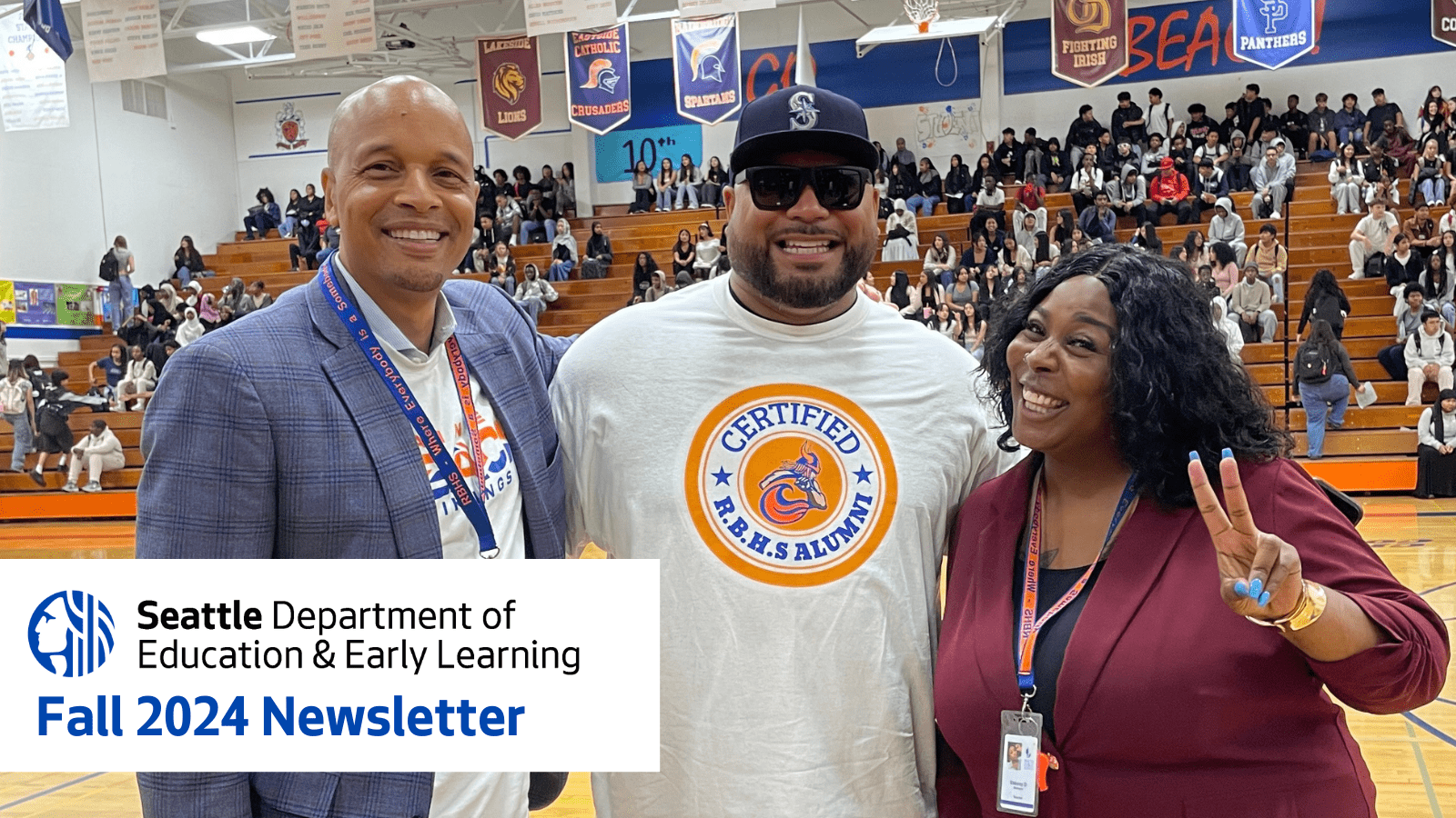 Wearing a gray suit, Dr. Dwane Chappelle stands with two school staff in the Rainier Beach High School gym on the first day of school