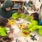 Preschool children paint with their hands while their teacher leads them.