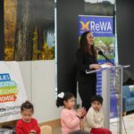 Mayor at the podium with three children sitting.