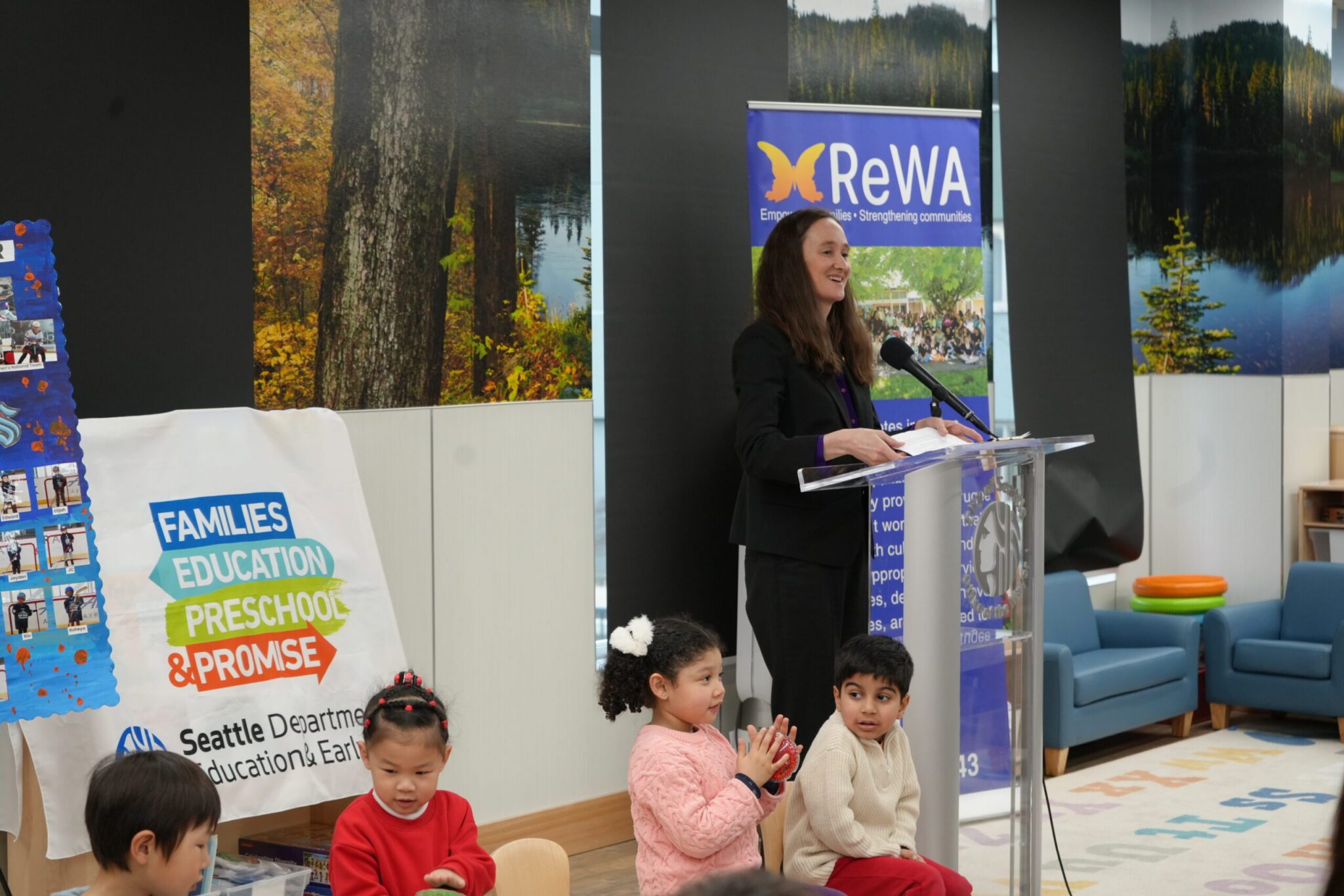 Mayor at the podium with three children sitting.