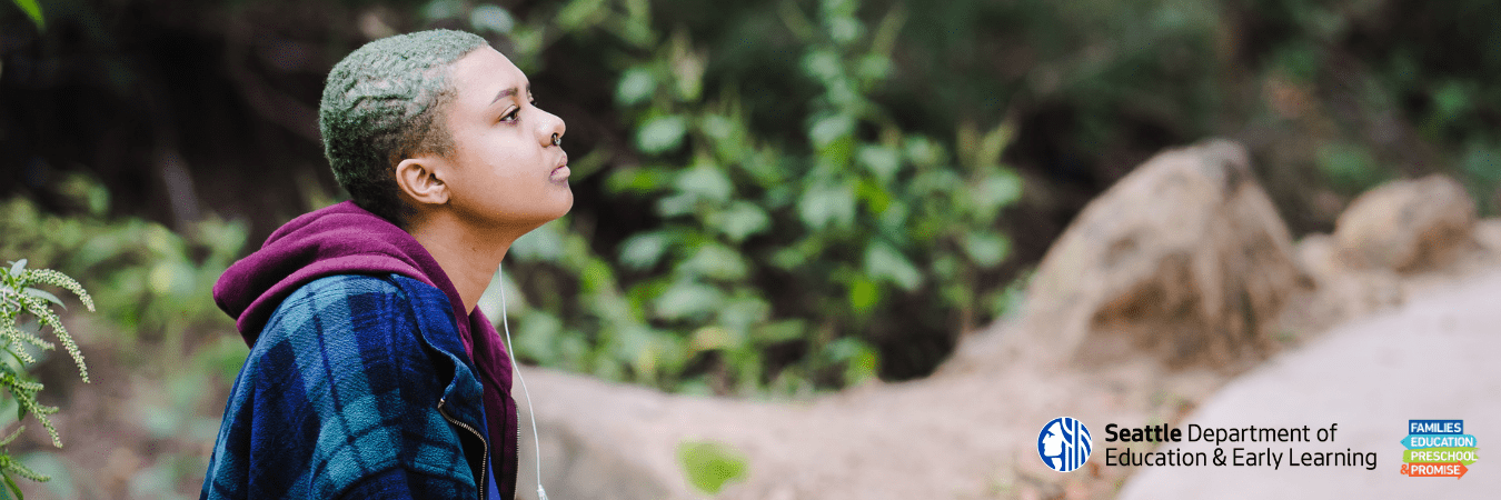 Profile of a high school aged youth of color wearing a plaid shirt sitting outdoors